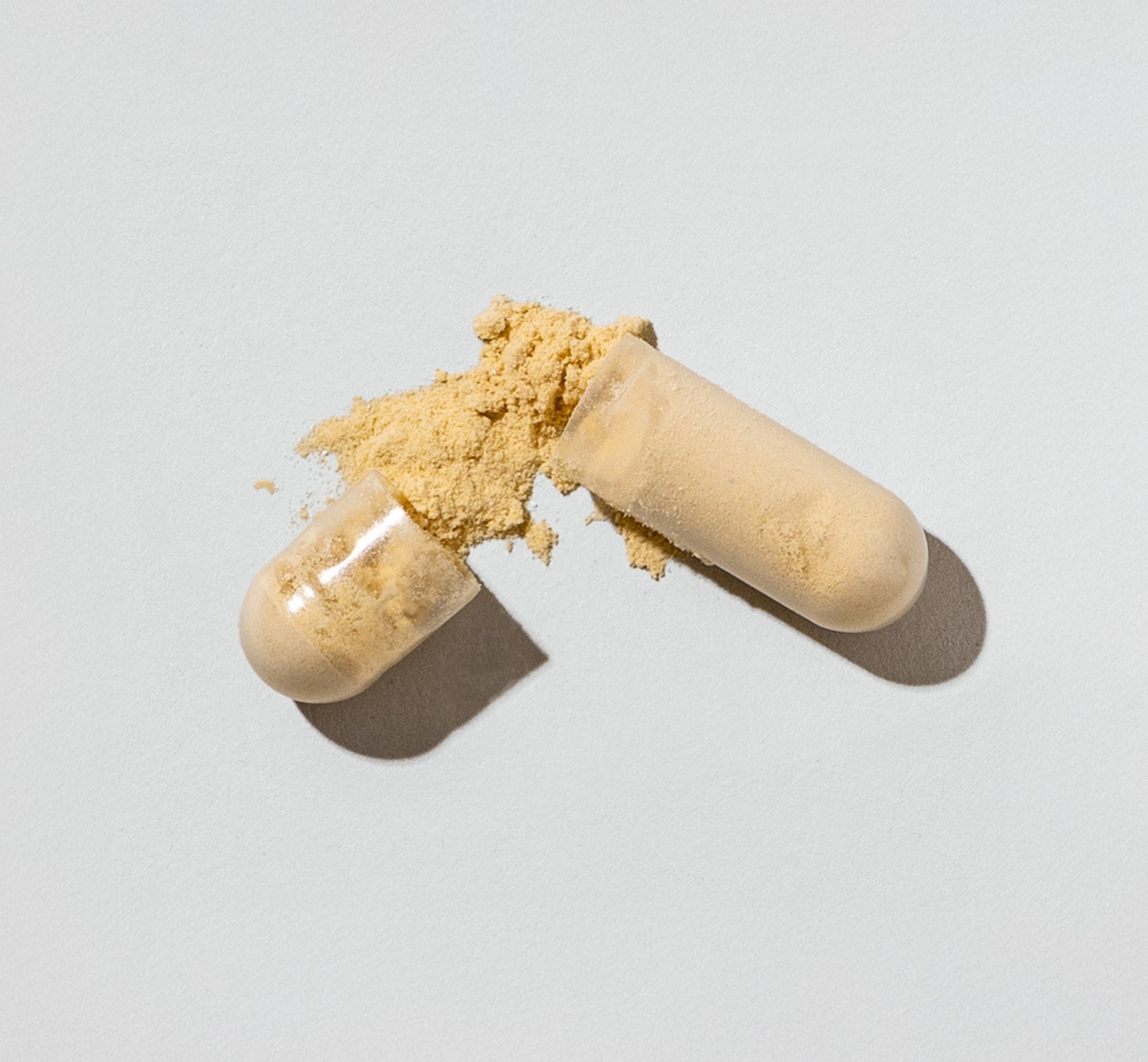 Two capsules with yellow powder spilling out on a light gray background