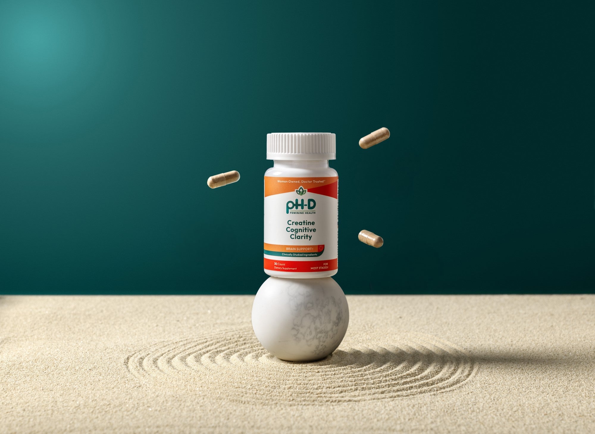 Bottle of pH-D Creatine Cognitive Clarity on a sand-like surface with a teal background