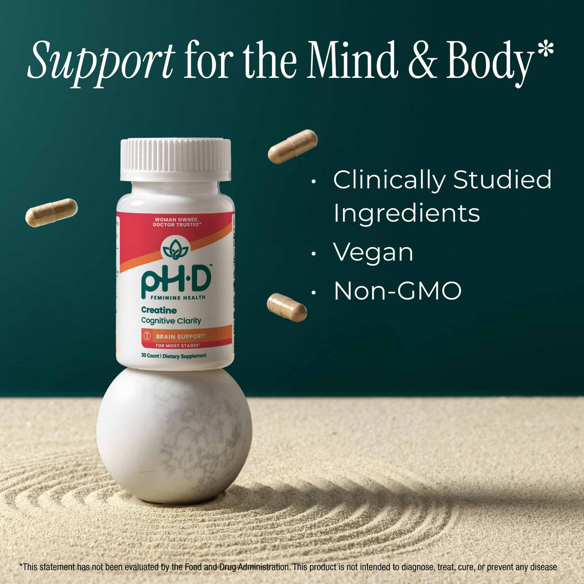 A bottle of pH-D Creatine Cognitive Clarity dietary supplement stands on a white marble sphere in a styled studio scene with sand ripples and floating capsules. Text on the image reads 'Support for the Mind & Body' and lists benefits: clinically studied ingredients, vegan, non-GMO.