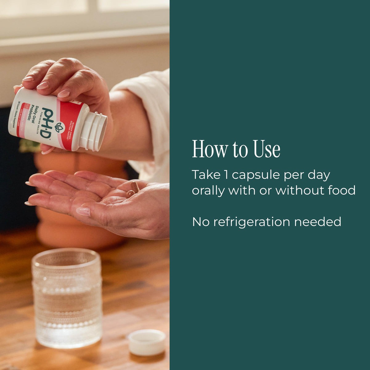 A person holds an open white bottle of pH-D Feminine Health Daily Oral Probiotics and pours capsules into their palm. A glass and the bottle cap sit on a wooden table.