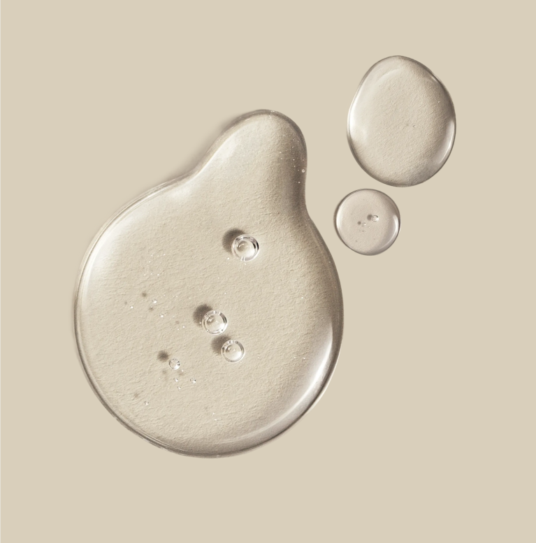 Three translucent droplets of clear gel or serum on a warm beige background.